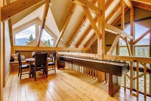 A wooden interior with a high ceiling, a billiards table, and large windows offering a view of the outdoors.