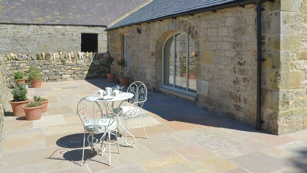 A stone building with a tiled patio, a table with chairs, and potted plants.