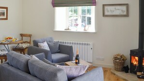 A living room with a grey sofa, a table with a bottle and glasses, a fireplace, and a window with a view of greenery.