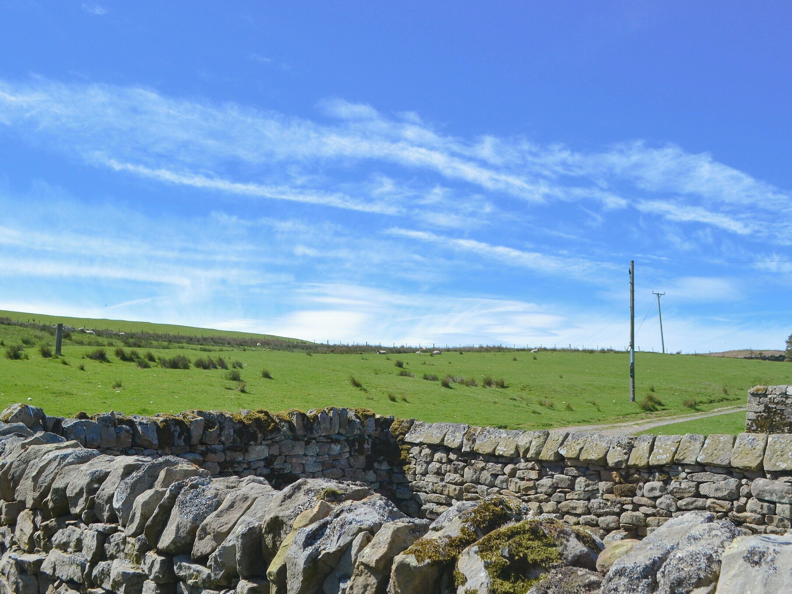 A stone wall with a grassy field and a clear sky.