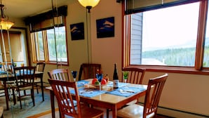 Comedor con mesa y sillas de madera, una botella de vino y una vista panorámica por la ventana.