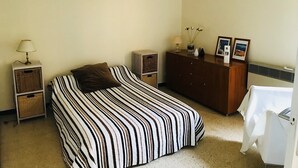 A bedroom with a striped bed, a dresser, a lamp, and a radiator. - Bright apartment T3 ideally located for a holiday by the sea (Saint-Cyprien)