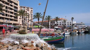 A marina with boats, a rock fountain, and buildings with shops and restaurants. - Bright apartment T3 ideally located for a holiday by the sea (Saint-Cyprien)