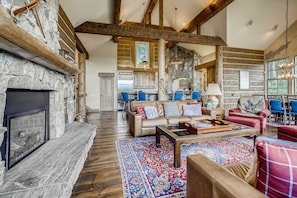 A spacious living area with a stone fireplace, wooden beams, and a large window. - Estate on 5 acres | 3.5 mi to Main St | Hot Tub! (Breckenridge)