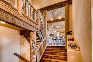 Staircase leads to a dining area with wooden chairs and tables, and a stone fireplace in the background.
