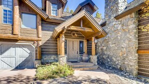Une cabane en rondins avec une cheminée en pierre, une porte d’entrée en bois et un garage.