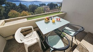 En balkong med ett bord och några stolar, en korg med frukt och ett glas apelsinjuice.