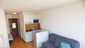 Ett kompakt bostadsutrymme med ett litet kök, en soffa och en dörr som leder till ett annat rum.