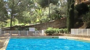 En rektangulär swimmingpool omgiven av ett vitt staket, med träd och en stenmur som bakgrund.
