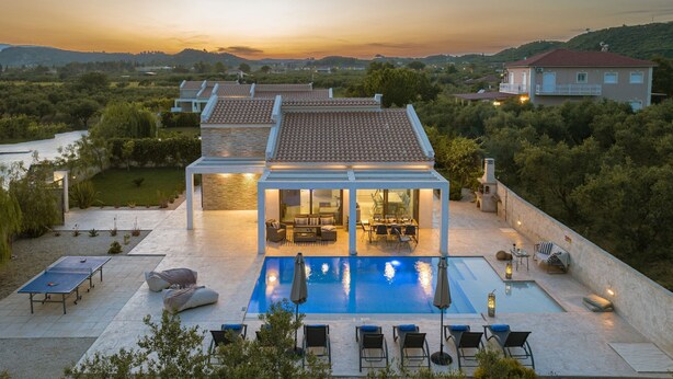 Eine moderne Villa mit Swimmingpool, Sitzgelegenheiten im Freien und Blick auf die umliegende Landschaft.