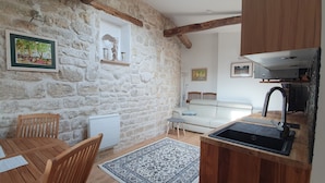 A cozy room with a stone wall, a wooden table with chairs, a sofa, and a kitchen area with a sink and cabinets. - Warm appartment in the center of historical Paris with full equipment (Paris)