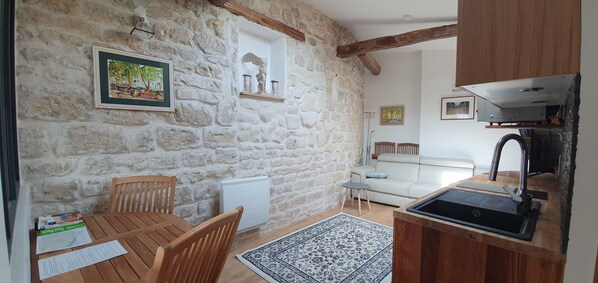 Una habitación acogedora con una pared de piedra, una mesa de madera con sillas, un sofá y una zona de cocina con un lavabo y armarios.
