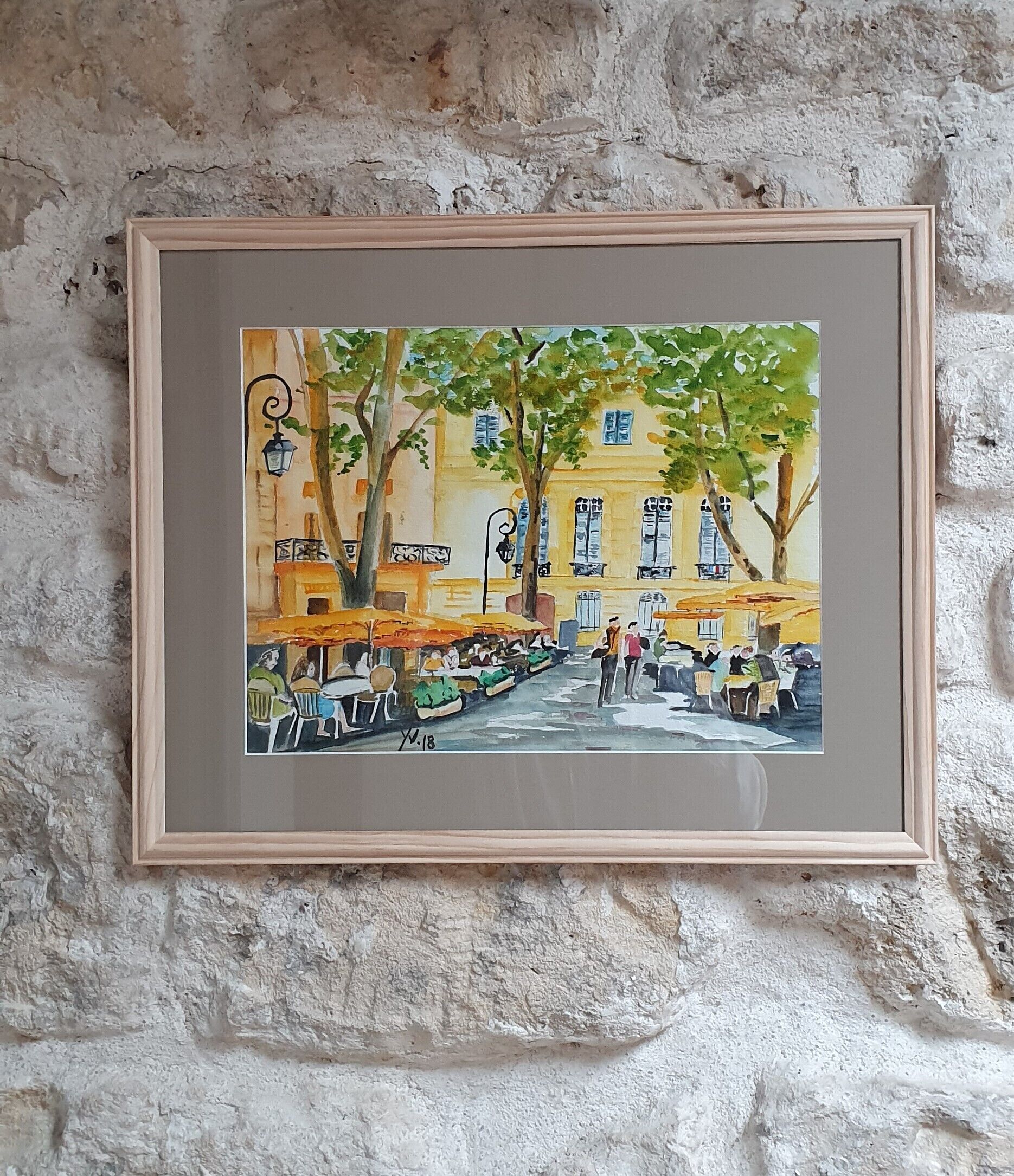 Een lijst met een schilderij van een straatbeeld met gebouwen, bomen en mensen.