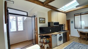 A compact kitchen with a microwave, sink, and washing machine, a dining area with a table and chairs, and a large window providing natural light. - Warm appartment in the center of historical Paris with full equipment (Paris)