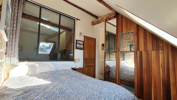 A bedroom with a large window, wooden wardrobe, and a bed with patterned bedding. - Warm appartment in the center of historical Paris with full equipment (Paris)