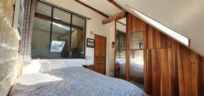 Une chambre dotée d’une grande fenêtre, d’une armoire en bois et d’un lit avec une literie à motifs.