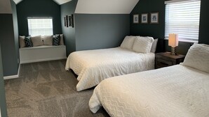 Un dormitorio con dos camas, un banco con almohadas, una lámpara y cuadros en la pared.