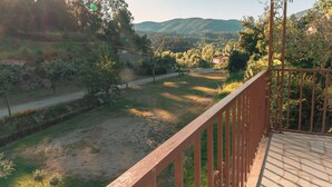 Ein Balkon mit Blick auf eine ländliche Landschaft, darunter Bäume, eine Straße und ferne Hügel.