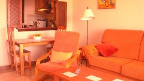 A living room with a sofa, a dining table with chairs, a kitchen area with a stove, and a painting on the wall. - FIRST LINE BEACH LUXURY APARTMENT. SEA VIEWS (Ayamonte)