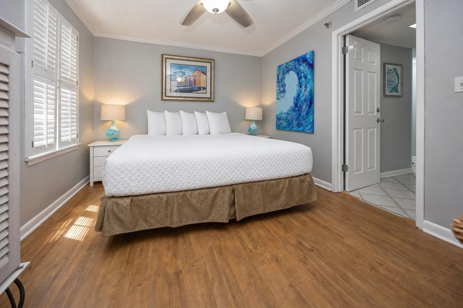 A bedroom with a bed, two bedside tables, a ceiling fan, and artwork on the walls.