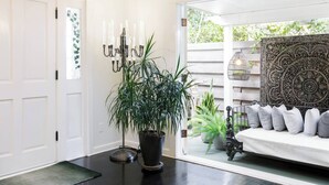 Une pièce avec un sol noir, des murs blancs, une porte blanche, une plante en pot, un chandelier et une décoration murale à motifs.