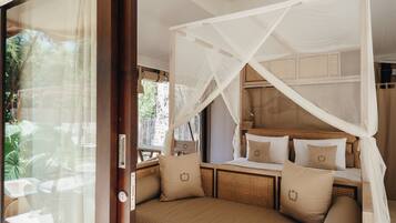 A room with a bed under a canopy, a window with curtains, and a view of greenery outside.