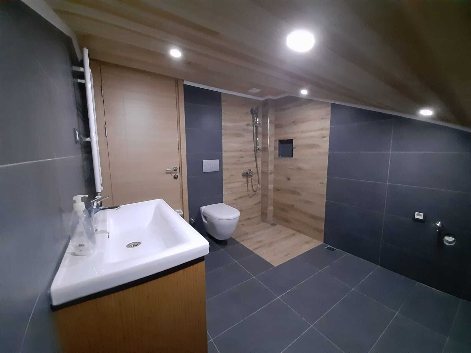 A modern bathroom with a wooden vanity, a shower, and a toilet.