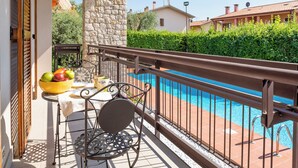 Un balcón con una silla de metal, una mesa con un cuenco de fruta y una piscina.