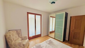 Un dormitorio con cama, una silla, armario y puerta.