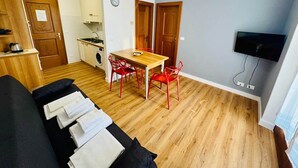 Un espacio habitable compacto con kitchenette, comedor y televisor montado en la pared.