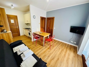 A compact living space with a kitchenette, dining area, and a TV mounted on the wall.