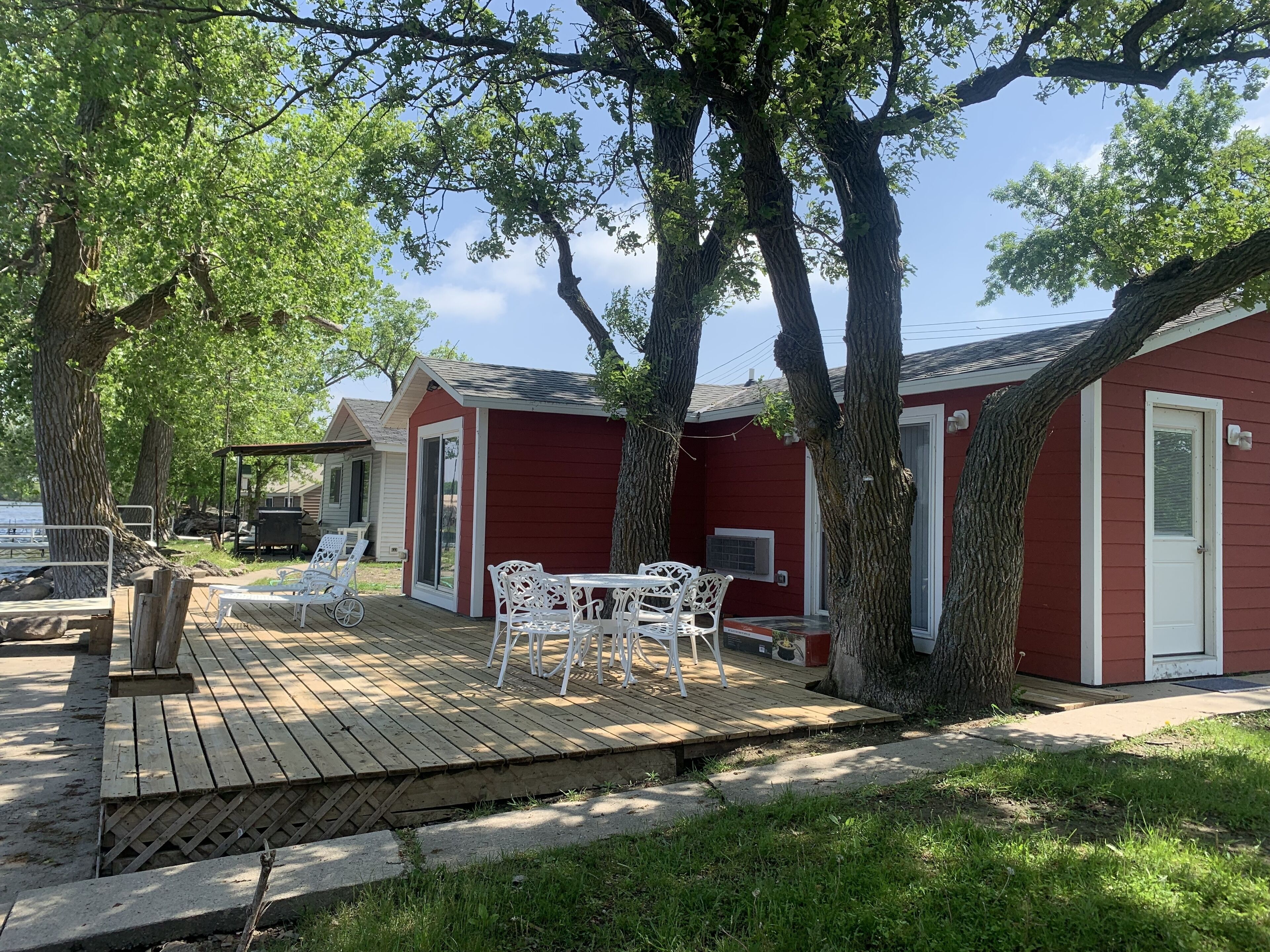A wooden deck with outdoor furniture, a red building with a white door, and trees.