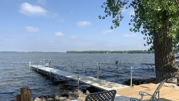 Eine Holzterrasse mit Metallstühlen und einem kleinen Steg, der in einen See führt.