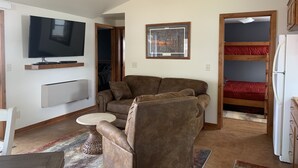 Ein gemütlicher, kleiner Wohnraum mit Sofa, Fernseher, einem gerahmten Bild, einem Etagenbett und einem Kühlschrank.