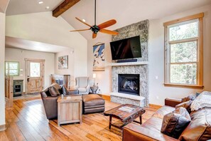 A spacious living room with a stone fireplace, leather furniture, a ceiling fan, and a television mounted above the fireplace.