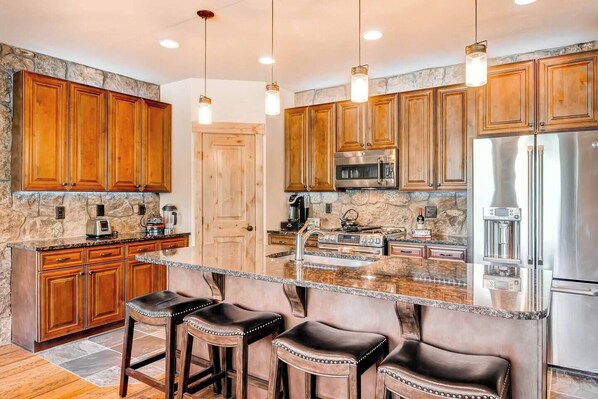 A kitchen with wooden cabinets, a central island with stools, a built-in oven, and a refrigerator.