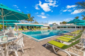 A pool area with lounge chairs and umbrellas, a clear blue sky, and palm trees.