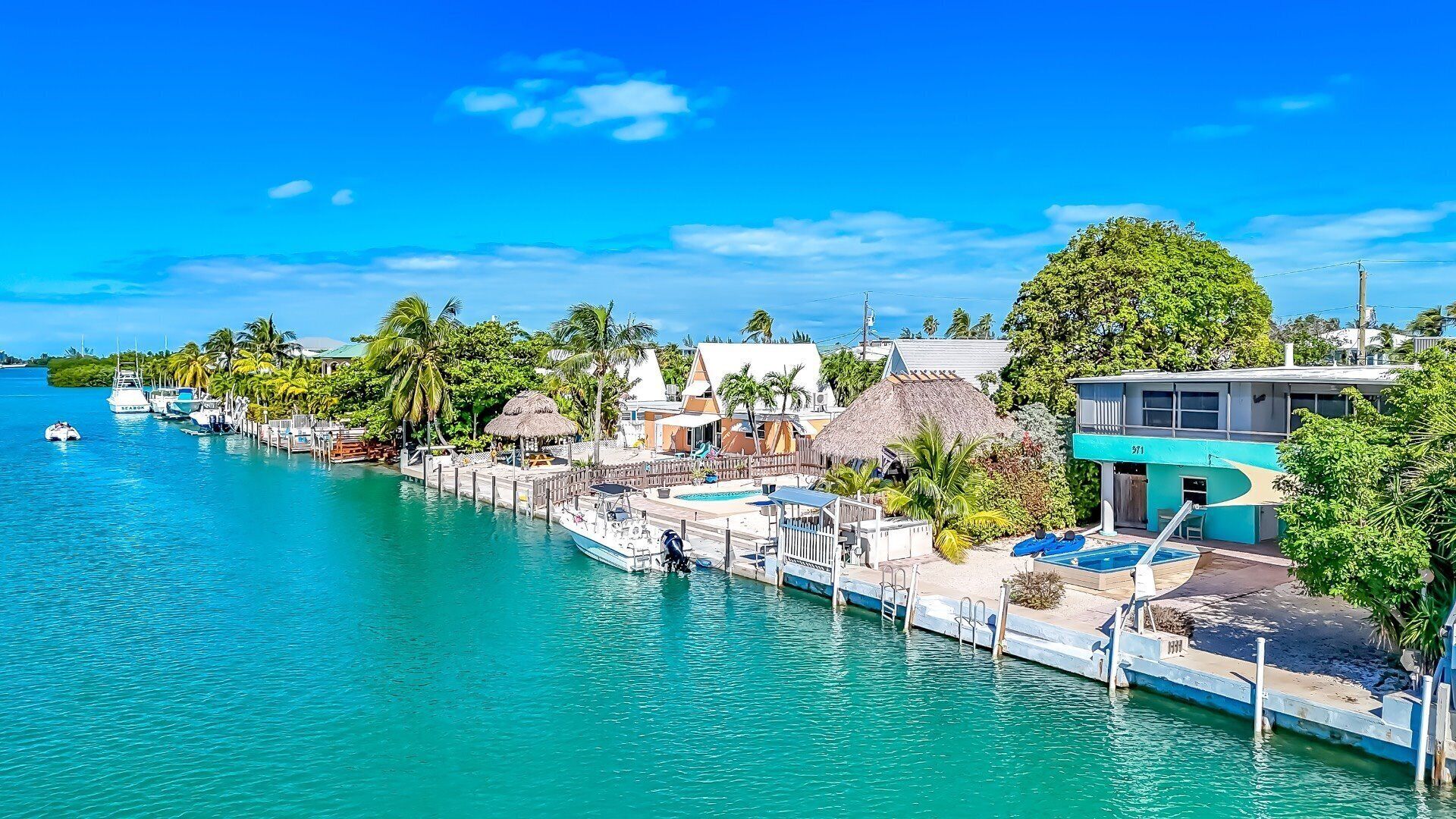 A coastal resort with a dock, swimming pool, and thatched-roof structures.