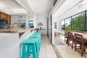 A kitchen with a granite countertop, a stainless steel sink, and wooden cabinets. There are turquoise stools and a wooden dining table with chairs. - Welcome to A Taste of Vitamin Sea – Your Key Colony Beach Escape! (Key Colony Beach)