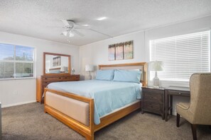 A bedroom with a bed, a desk, a chair, a ceiling fan, and artwork on the wall. - Welcome to A Taste of Vitamin Sea – Your Key Colony Beach Escape! (Key Colony Beach)