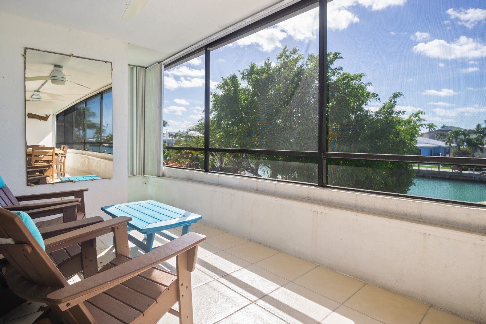 A balcony with a view of a body of water, a table, and chairs.