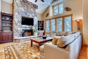 A living room with a stone fireplace, a flat-screen TV, a sofa, and a coffee table. - Gondola In/Out | Hot tub | Shock Hill Hideaway (Breckenridge)