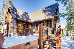 A log cabin with a hot tub, wooden deck, and a staircase leading to the entrance.