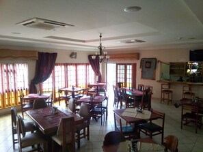 Restaurante com várias mesas e cadeiras de madeira, um espaço de bar e um ventilador de teto.