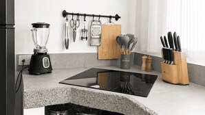 Et køkken med bordplade, blender, ophængte redskaber, et krydderihylder og en komfur.