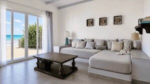 A modern living room with a sofa, a coffee table, and a view of the beach through large windows.