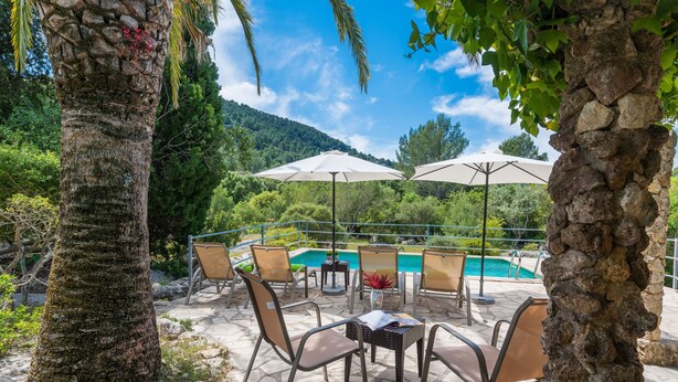 An outdoor seating area with stone tables and chairs, a pool, and umbrellas. - CAN COMPANY - Villa with private pool in Campanet. Free WiFi (Campanet)