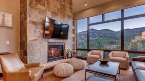Una sala de estar moderna con chimenea de piedra, sofás de cuero y ventanas amplias con vistas a la montaña.