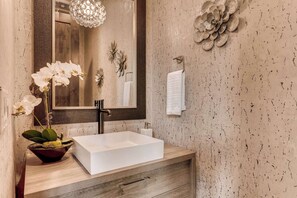 Une salle de bain avec un lavabo blanc, un miroir, un mur décoré de motifs floraux et un luminaire suspendu.