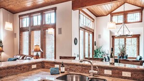 Una cocina con encimeras de granito, pileta de acero inoxidable, armarios de madera y ventanas amplias con persianas.